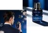 Perfume bottle labeled 'esse Spirit Blue' held by a person against a dark background.